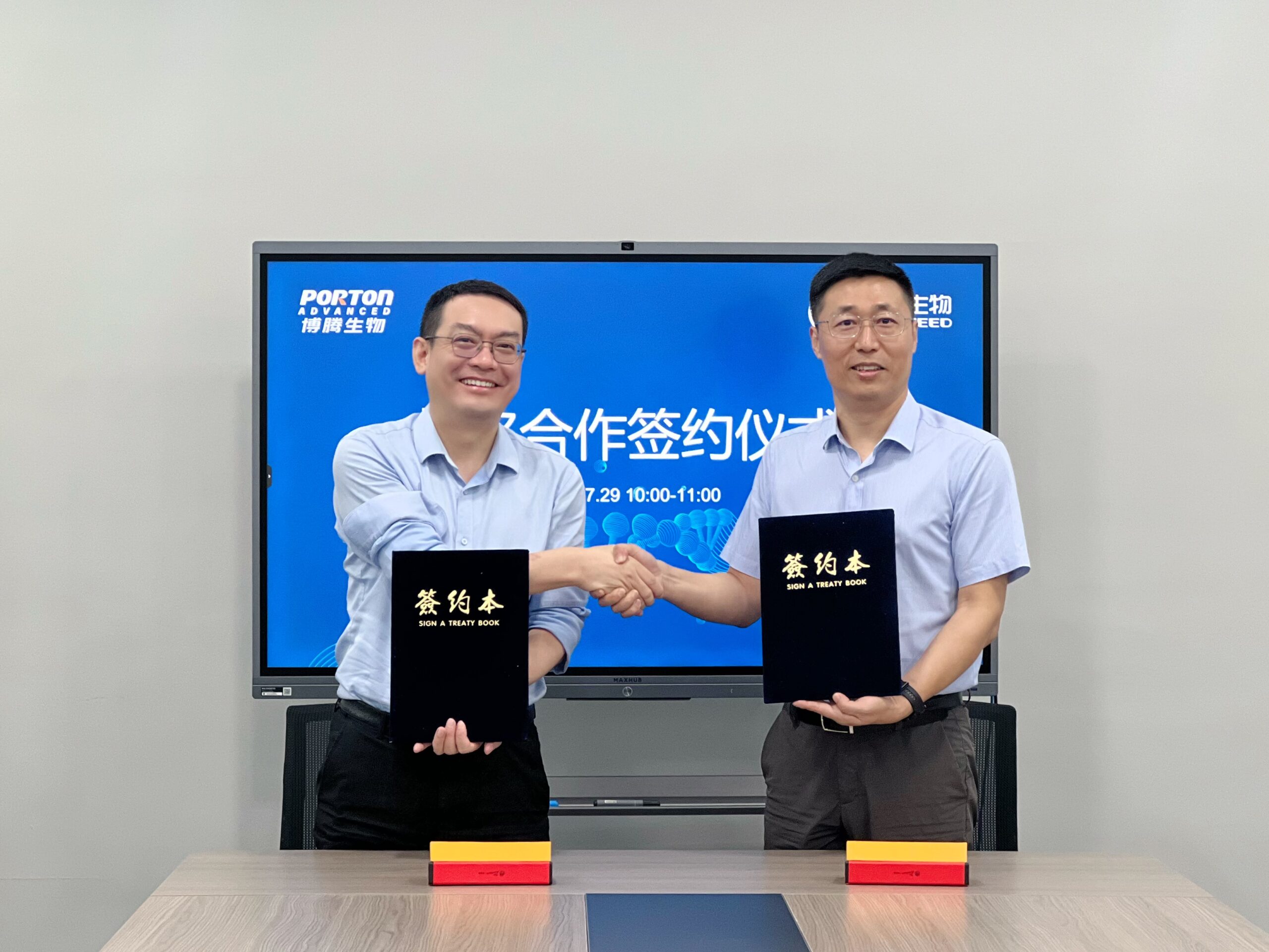 Two men in shirts shake hands and hold black folders, marking a significant signing event in front of a large screen displaying text in Chinese, hinting at the collaboration between Porton Advanced and Geneseed Biotech for circRNA Innovative Therapeutics.